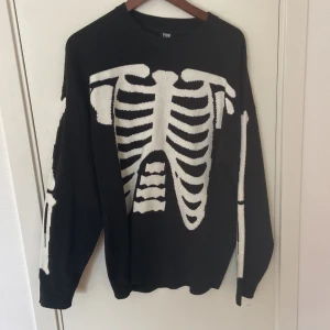 Svart stickad tröja med skelett FSBN - Cool svart stickad tröja från FSBN i relaxed fit med stort vitt skelettmönster på både fram- och baksida samt ärmar. Perfekt för dig som gillar edgy och unik stil. Rund hals och långa ärmar, passar dig som vill sticka ut.