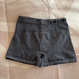 Grå träningsshorts SWEDEN COUNT - Säljer ett par grå, tighta träningsshorts från SWEDEN COUNT. De är gjorda i mjukt, stretchigt syntetmaterial som sitter skönt mot kroppen. Perfekta för gymmet eller sport. Diskret logga i svart på linningen.
