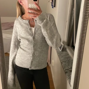 Grå stickad kofta från 157 - Mysig grå stickad kofta från 157 med rund hals och knappar hela vägen framtill. Koftan har långa ärmar och ribbade muddar vid ärmslut och nederkant. Perfekt att slänga på sig när det är lite kyligt ute.