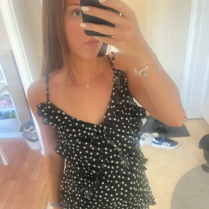 Prickig volangklänning - Säljer en svart klänning med vita prickar och volangdetaljer från H&M. Klänningen har smala axelband och är ärmlös, perfekt för varma dagar. Lätt och luftig modell som ger en söt och trendig look. Använd endast två gånger!