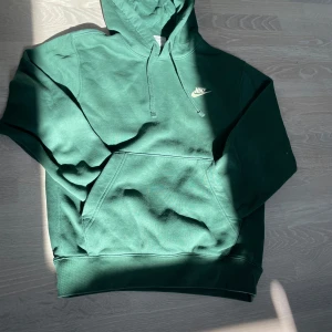 Grön hoodie från Nike  - Säljer en grön Nike hoodie i storlek XS med klassisk broderad logga på bröstet. Tröjan har huva med snörning och en stor magficka. Mjuk insida i fleece och ribbade muddar vid ärmslut och nederkant. 