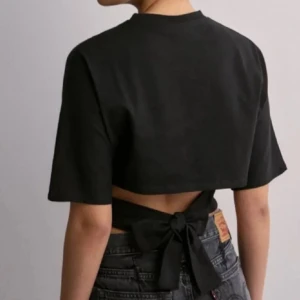 Svart croppad topp med knyt i ryggen - Säljer dem populära knyt toppen från Nelly i storlek xs🩷 den är knappt använd och är som ny, Inga fläckar eller hål💓