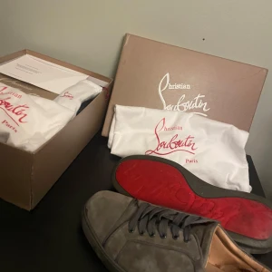 Grå sneakers från Christian Louboutin - Säljer ett par grå sneakers från Christian Louboutin med den ikoniska röda sulan. Skorna har rund tå, snörning och är tillverkade i mocka med läderfoder. Kommer med originalkartong och dustbags. Perfekt för dig som gillar lyxiga detaljer och stilren design. Priset kan gå ner vid snabb affär!