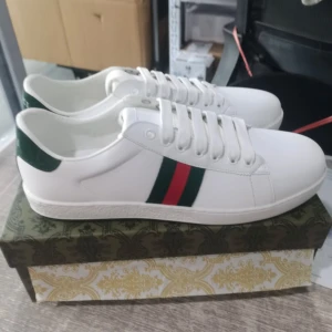 Gucci ace sneakers - Säljer ett par vita feeeta gucci ace skor. Box och dustbag m.m ingår med skorna. De är oanvända. Vid frågor är det bara att ställa!