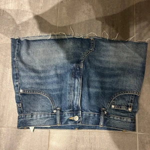 Blå jeanskjol med rå kant - Säljer en cool kort jeanskjol i klassisk blå denim med rå, fransig kant upptill. Kjolen har framfickor, bakfickor och bälteshällor, samt en knapp och dragkedja framtill. Low waist 