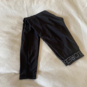 Svarta leggings från Maya Delorez - Snygga svarta leggings från Maya Delorez med bred resår i midjan där loggan syns tydligt. De är tighta och gjorda i ett stretchigt syntetmaterial som passar perfekt till träning eller chill. Stilrena sömmar och diskret logga på benet.