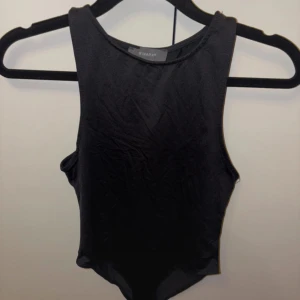 Svart ärmlös topp från Primark - En stilren svart ärmlös topp från Primark i storlek XS. Toppen har hög halsringning och är figurnära med en enkel, clean design. Perfekt att matcha med jeans eller kjol för en snygg look.