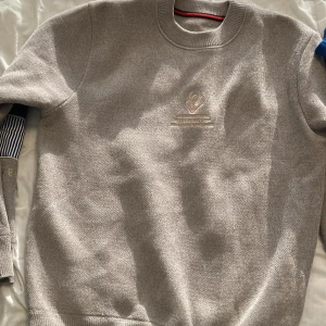 Grå tröja med broderi från cutebut - Snygg grå tröja från cuteboy med broderad logga på bröstet. Ärmarna har coola detaljer med mörkblå tygpatch och randigt tyg i vitt och blått. Rund hals och ribbade muddar. Perfekt för dig som gillar unika detaljer och stilren design. Storlek på den är M-L