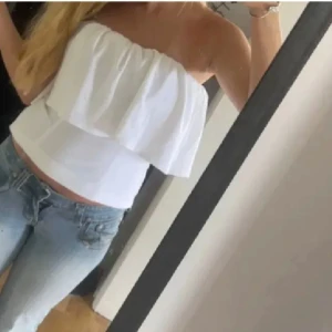 Vit slutsåld bandeau tubtopp med volang från Zara - Säljer en fräsch vit bandeau tubtopp med bred volang upptill. Toppen är axelbandslös och sitter tight runt kroppen, perfekt till jeans eller kjol. Enkel och stilren design som passar till många olika looks.