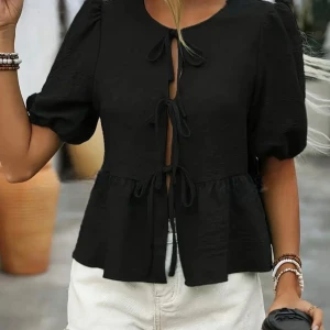 Svart blus med knyt och puffärm - Trendig svart blus med korta puffärmar och flera knyt framtill som ger en cool och unik look. Blusen har en lätt utsvängd passform nedtill och rund halsringning. Perfekt för dig som vill sticka ut med snygga detaljer.