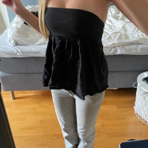 Svart bandeau tubtopp - Säljer en svart bandeau tubtopp med volym och lätt rynkad nederdel. Toppen är axelbandslös och har en luftig, flowy passform som ger en cool och avslappnad vibe. Perfekt att styla med jeans eller kjol för en trendig look.
