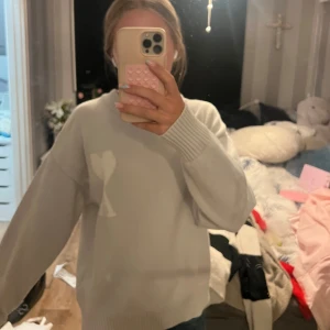 Ljusgrå stickad tröja från Ami - Säljer en ljusgrå stickad tröja från Ami med deras ikoniska hjärta och A-logga på bröstet. Tröjan har en loose fit, långa ärmar och breda ribbade muddar. Perfekt för dig som gillar stilren och trendig design. Endast blivit andvänd en gång och var inte min stil derför säljar jag den 