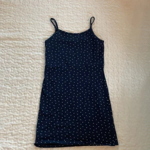 Mörkblå prickig klänning H&M - Supersöt mörkblå kortklänning från H&M med vita prickar och smala axelband. Tillverkad i mjuk ekologisk bomull, perfekt för varma dagar. Enkel och stilren modell som är lätt att matcha med sneakers eller sandaler. Perfekt till att sy om till kjol/topp.