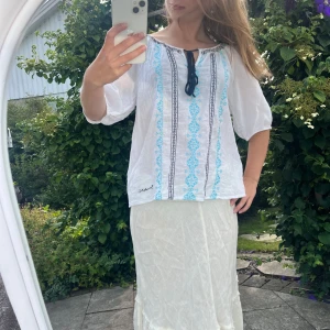 Söt blus  - Söt blus från Bondelid, size S, fint skick förut om att en ”tofs” i banden där fram har lossnat, man kan klippa bort banden om man vill. Pris 90kr. Blusen är vit och har turkosa, mörkblåa & svarta detaljer broderat. 