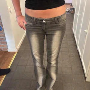 Grå bootcut jeans med låg midja - Säljer ett par grå jeans med snyggt slitna detaljer och bootcut-modell. Byxorna har låg midja och klassisk femficksdesign. Perfekta för dig som gillar en avslappnad men trendig look.