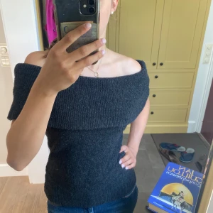 Mörkgrå offshoulder stickad tröja - Snygg mörkgrå stickad tröja med offshoulder-design och bred krage som vilar över axlarna. Modellen är tight och sitter fint mot kroppen, perfekt för dig som gillar en stilren look med lite edge. Materialet är mjukt och värmande, passar till jeans eller kjol.