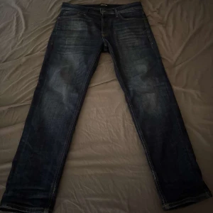 blå jeans från Jack & Jones - Snygga blå jeans från Jack & Jones med klassisk femficksdesign och diskreta slitningar framtill. Jeansen har raka ben och normal passform, perfekta till sneakers eller boots. Tillverkade i slitstarkt bomullsjeansmaterial.