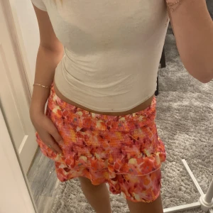 Färgglad blommig volangkjol - Säljer en kort kjol med blommigt mönster i rosa, orange och rött.