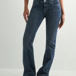 Blå bootcut jeans med broderade fickor - Snygga blå jeans med bootcut passform och coola broderade detaljer på bakfickorna. Klassisk femficksmodell med normal midja och dragkedja. Jeansen har en mörk tvätt och är tillverkade i mjukt denimtyg som sitter skönt hela dagen. Använd 4ggr 