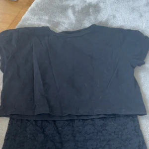 Svart spetsklänning från Gina Tricot - Säljer en svart klänning från Gina Tricot i storlek 146/152. Klänningen har ärmlös design och är täckt av snygg spets med blommigt mönster. Perfekt för dig som gillar en stilren look med lite extra detaljer.