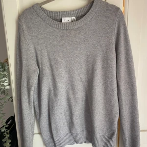 Grå stickad tröja från VILA - Snygg grå stickad tröja från VILA i storlek S. Tröjan har rund halsringning och ribbade muddar vid ärmslut och nederkant. Perfekt för dig som gillar enkel och stilren design med mjukt material och långärmad passform.