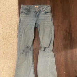Ljusblå bootcut jeans med slitningar - Säljer ett par ljusblå bootcut jeans från Mavi med slitna detaljer på knäna och broderade bakfickor med färgglada zigzag-mönster. Jeansen har klassisk femficksdesign och är tillverkade i mjukt denimtyg. Perfekta för en avslappnad och trendig look. NYPRIS LIGGER P 700kr