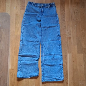 Blå wide jeans med raka ben - Säljer ett par blå jeans med bred passform och raka ben. Byxorna har hög midja, klassisk dragkedja och knapp framtill samt stora bakfickor. Materialet är en mix av bomull, polyester och elastan för lite stretch. Perfekta för en avslappnad och trendig look.