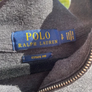 Grå quarter zip tröja från Polo Ralph Lauren - Snygg mörkgrå långärmad tröja från Polo Ralph Lauren med half zip och klassisk broderad logga på bröstet. Tröjan är ribbad och gjord i mjuk bomull, perfekt för chill dagar. Passar dig som gillar stilrena och tidlösa plagg med premiumkänsla. Kom gärna med bud MVH/ Casper