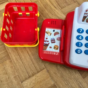 Kassa - Ingen bok syns på bilderna, utan det är en leksakskassaapparat med tillhörande varukorg, mynt och kort. Perfekt för att leka affär och träna på att räkna och hantera pengar. Färgglad och rolig för unga som gillar rollspel och shopping.