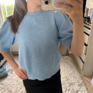 Ljusblå stickad tröja Vero Moda - Superfin ljusblå stickad tröja från Vero Moda med korta puffärmar och rund halsringning. Tröjan har en mjuk och mysig känsla, perfekt för lager på lager. Ribbstickade detaljer vid ärmslut och nederkant ger en snygg finish.