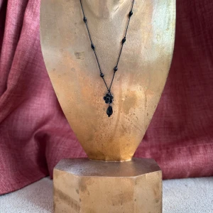 Svart halsband med blomma och pärla - Unikt svart halsband med en cool blomformad hängare och en svart droppformad pärla. Halsbandet har svarta pärlor längs snöret och ger en mystisk vibe. Perfekt för dig som gillar detaljer och vill  ut med en snygg accessoar.