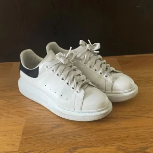 Alexander mqueen skor - Stilrena vita sneakers från Alexander McQueen med svart hälparti och tjock sula. Skorna har rund tå, snörning och är tillverkade i skinn. Perfekta för dig som gillar en clean och modern look med exklusiv känsla.