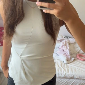 Vit ärmlös topp från BikBok  - Säljer en stilren vit ärmlös topp från BikBok i storlek XS. Toppen har en asymmetrisk sömdetalj framtill som ger en snygg twist och är tillverkad i ett mjukt, stretchigt material. Perfekt att matcha med jeans eller kjol för en clean look.