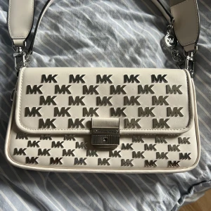 Michael Kors handväska - Vit handväska med silvriga detaljer. Den går att bära över axeln, men kommer även med ett längre band. Har ett stort fack och två mindre på insidan, samt ett på baksidan. Väskan är köpt på Michael Kors i Stockholm och nypris är ca 3 tusen. Använd någon enstaka gång och är i mycket fint skick. Säljs för 850kr. 