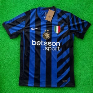 Inter Milan matchtröja Nike blå/svart - Inter Milan fotbollströja från Nike med klassiska blå och svarta ränder, klubbmärke och sponsortryck på bröstet. Tröjan har korta ärmar, V-ringning och är tillverkad i lätt, ventilerande polyester. Perfekt för dig som vill visa ditt stöd för Inter.