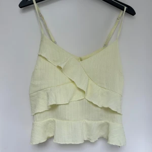 Ljusgul volangtop från SHEIN - Supersöt ljusgul linnetopp från SHEIN med justerbara smala axelband ochvolanger fram och baktill. Toppen har en lätt strukturerad yta och dragkedja i sidan. Aldrig använd