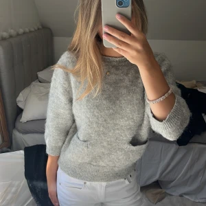 Grå stickad tröja från Zara - Mysig grå stickad tröja från Zara med rund halsringning och trekvartsärmar. Tröjan har en fluffig känsla och ribbade muddar vid ärmslut och nederkant. Ger en look av mohair. Klicka gärna på ”köp nu”!