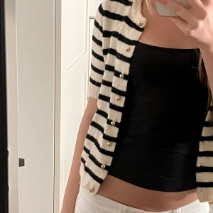 Randig kofta från H&M i XS - Superfin kortärmad kofta från H&M i storlek XS. Koftan är vit med svarta ränder, har rund halsringning och knäpps med små knappar framtill. Perfekt att slänga över en topp för en chill och trendig look.