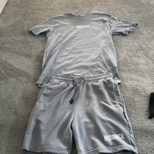 Grå shorts från Hoodrich med snörning - Snygg grå tracksuit från Hoodrich med vit logga tryckt på benet o bröstet. De har en relaxed fit och justerbar snörning i midjan för extra komfort. Perfekta för chill dagar eller när du vill ha en clean streetwear-look.