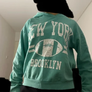 Turkos hoodie med New York-tryck Kappahl - PRIS KAN DISKUTERAS💕💕💕 Turkos hoodie från Kappahl med vit text 'NEW YORK BROOKLYN' och amerikansk fotbollstryck på bröstet. Mjuk insida, huva och ribbade muddar. Långärmad och i skönt bomullsmaterial. Lite lim på armen bak men inget som märks, bild finns i annonsen!