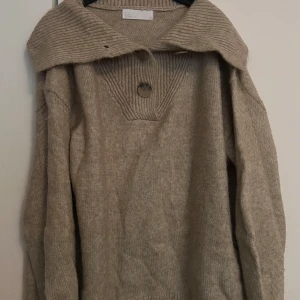 Beige stickad tröja - Beige stickad tröja med stor ribbad krage och tre knappar framtill. Mjuk och skön i materialet, sticks inget alls.