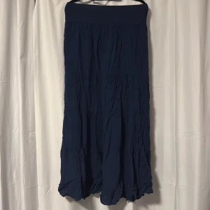 Mörkblå långkjol med resårmidja - Säljer en mörkblå långkjol med bred resår i midjan. Kjolen har ett lätt skrynklat tyg och är enkel i modellen utan mönster eller extra detaljer. Perfekt för dig som gillar en stilren och bekväm look.