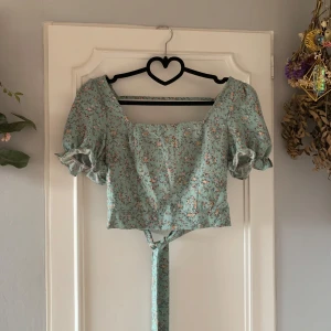 Blommig croppad blus från Shein - Söt blommig croppad blus från Shein i mintgrön färg. Blusen har korta puffärmar och knytband i bak samt en öppen rygg. Perfekt för en somrig look!