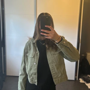 Grön croppad jacka - Säljer en snygg grön croppad jacka med knappar framtill. Jackan har en normal passform och långa ärmar, perfekt för vår och höst. Säljer pga vill att den ska få mer användning.