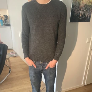 Grå stickad tröja från Ralph Lauren - Säljer en stilren grå stickad tröja från Ralph Lauren. Tröjan har en klassisk rund halsringning och långa ärmar med ribbade muddar. Perfekt för sommarkvällar och enkel att matcha med olika outfits. Ny pris: 2000kr. Skick 8/10