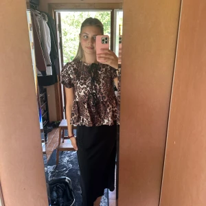 Leopardmönstrad blus med svart kjol - Snygg leopardmönstrad blus med korta ärmar och knytband i halsen. Matchas med en elegant svart långkjol. Perfekt för en trendig look. Endast testad
