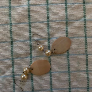 Beige örhängen med pärldetaljer - Säljer ett par unika örhängen med två pärlor och en oval beige platta🌸🌸