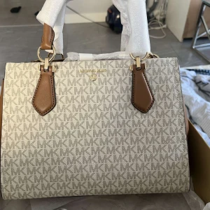  Michael Kors hand väska  - Säljer en snygg handväska från Michael Kors i beige med bruna detaljer och guldiga metalldelar. Väskan är köpt för 3500kr