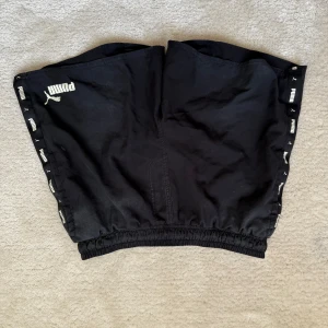 Svarta badbyxor från Puma - Säljer ett par svarta badbyxor från Puma med elastisk midja och logotypdetaljer längs sidorna. Perfekta för en avslappnad stil. 