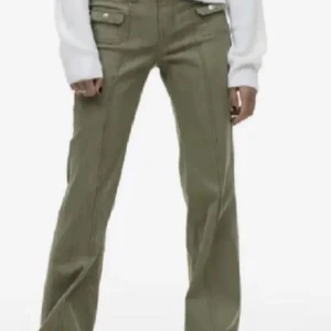 Olivgröna bootcut byxor med fickdetaljer - Snygga olivgröna byxor med bootcut-passform och markerade sömmar. Byxorna har två fickor framtill med lock och knappar, samt låg midja. Perfekta för en trendig vardagslook. Ifrån h&m i storlek 38